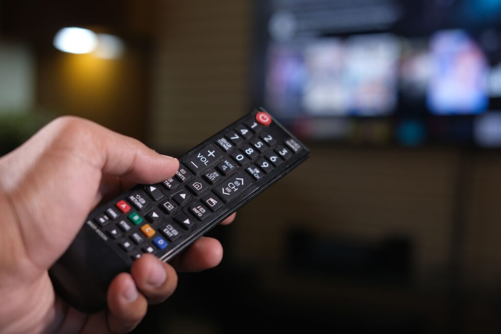 pexels-photo-11594553-11594553 Person holding a remote control with a blurred TV screen in the background.