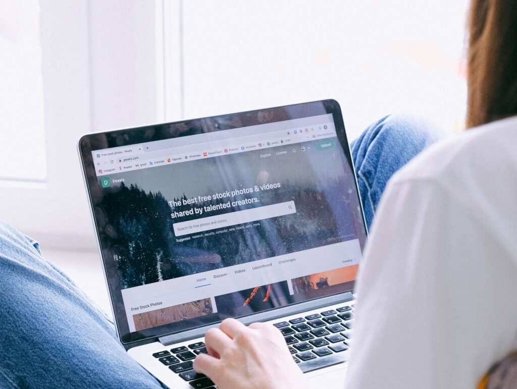 Young woman in casual jeans working on a laptop indoors by a window, showcasing remote work.
